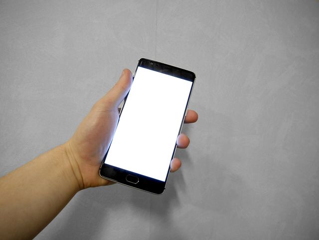 Hand holding smartphone with blank white screen.