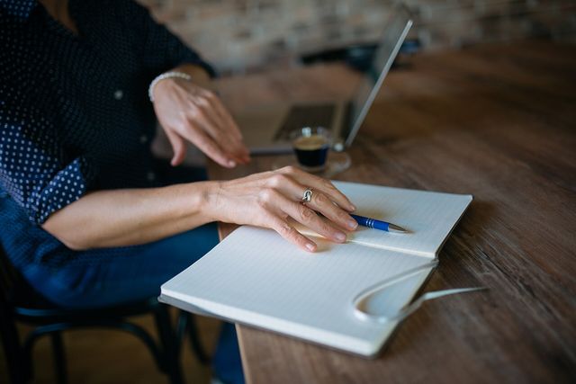 Close-up of a woman placing a pen on her notebook. Laptop and a cup of coffee in a blurry background