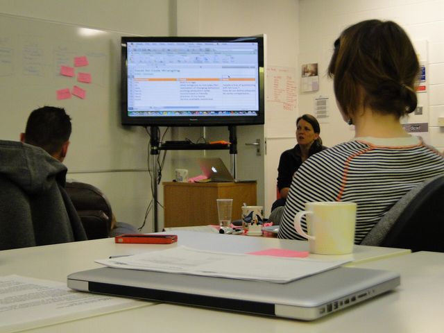 Students in front of large screen. In the foreground a closed laptop. Most likely qualitative data analysis in a spreads